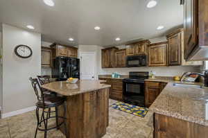 Kitchen with a kitchen island, sink, a breakfast bar area, black appliances, and light tile patterned flooring