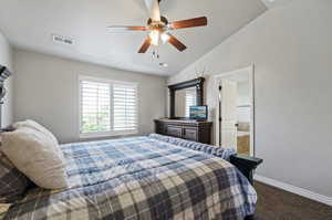 Bedroom featuring ceiling fan, carpet, vaulted ceiling, and ensuite bathroom