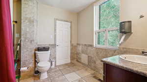 Bathroom with tile patterned floors, toilet, vanity, and tile walls