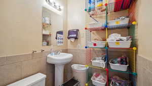 Bathroom featuring tile walls and toilet