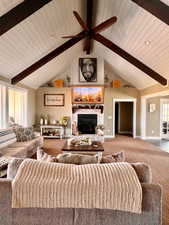 Carpeted living room with beamed ceiling, high vaulted ceiling, ceiling fan, and a brick fireplace