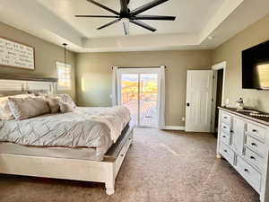 Bedroom featuring ceiling fan, a raised ceiling, access to outside, and light colored carpet