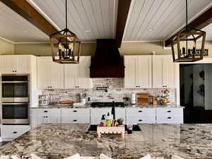 Kitchen with beamed ceiling, appliances with stainless steel finishes, hanging light fixtures, and premium range hood