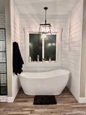 Bathroom with hardwood / wood-style flooring, shower with separate bathtub, wooden walls, and an inviting chandelier