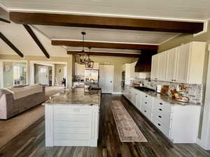 Kitchen with appliances with stainless steel finishes, beamed ceiling, a kitchen island with sink, white cabinets, and custom exhaust hood