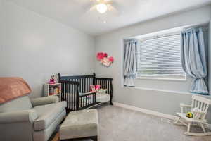 Carpeted bedroom featuring ceiling fan and a nursery area