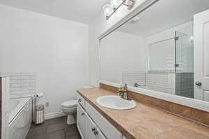 Bathroom featuring tile patterned floors, vanity, tiled bath, and toilet