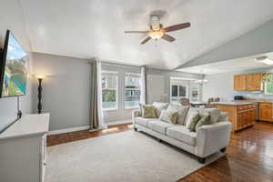 Living room with ceiling fan with notable chandelier, dark wood-type flooring, and lofted ceiling