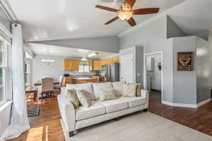 Living room featuring ceiling fan with notable chandelier, sink, dark wood-type flooring, and lofted ceiling