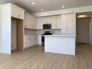 Kitchen with appliances with stainless steel finishes, light hardwood / wood-style flooring, a center island with sink, and white cabinetry (photos are not of actual home this is a previously built home)