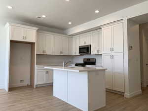 Kitchen featuring light wood-type flooring, white cabinetry, an island with sink, and stainless steel appliances (photos are not of actual home this is a previously built home)