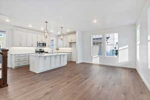 Kitchen with pendant lighting, a wealth of natural light, a center island with sink, and stainless steel appliances