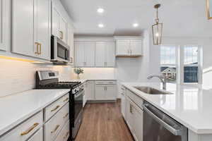 Kitchen featuring dark wood-type flooring, hanging light fixtures, sink, appliances with stainless steel finishes, and white cabinetry