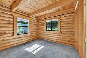 Carpeted spare room with beam ceiling, plenty of natural light, log walls, and wood ceiling