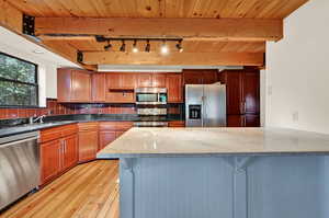 Kitchen featuring backsplash, appliances with stainless steel finishes, rail lighting, light hardwood / wood-style flooring, and wooden ceiling