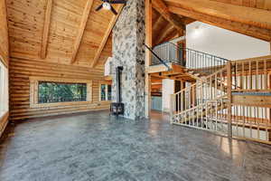 Unfurnished living room featuring high vaulted ceiling, beamed ceiling, a wood stove, ceiling fan, and wood ceiling