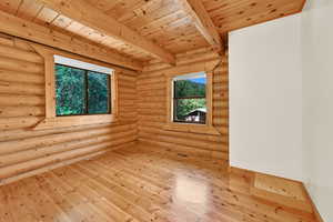 Spare room featuring rustic walls, light hardwood / wood-style flooring, beamed ceiling, and wood ceiling