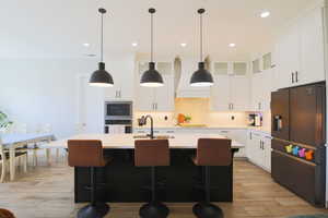 Kitchen with stainless steel refrigerator with ice dispenser, light hardwood / wood-style flooring, sink, and an island with sink