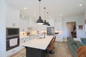 Kitchen with custom exhaust hood, sink, a center island with sink, stainless steel appliances, and light hardwood / wood-style floors