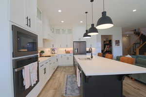 Kitchen with light hardwood / wood-style floors, a kitchen island with sink, sink, white cabinetry, and stainless steel appliances