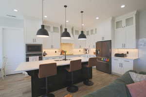 Kitchen with decorative light fixtures, a center island with sink, light hardwood / wood-style flooring, refrigerator with ice dispenser, and a breakfast bar area