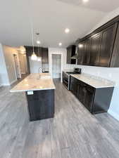Kitchen with sink, hanging light fixtures, double oven range, an island with sink, and wall chimney range hood