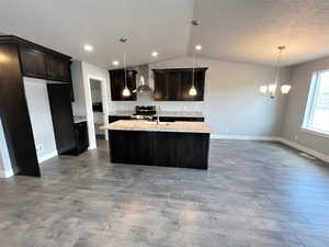 Kitchen featuring pendant lighting, wall chimney range hood, hardwood / wood-style flooring, a kitchen island with sink, and stainless steel range oven