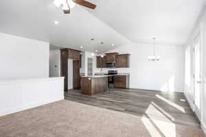 Kitchen featuring pendant lighting, lofted ceiling, dark brown cabinets, stainless steel appliances, and an island with sink