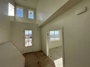 Entryway featuring light wood-type flooring, a towering ceiling, and a healthy amount of sunlight