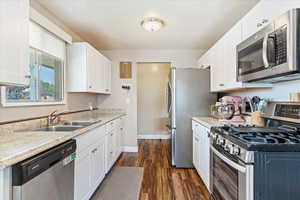 Kitchen with white cabinetry, appliances with stainless steel finishes, sink, and dark hardwood / wood-style floors