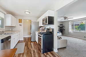 Kitchen with appliances with stainless steel finishes, sink, white cabinets, ceiling fan, and dark carpet