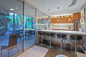 Kitchen featuring backsplash, pendant lighting, kitchen peninsula, stainless steel fridge, and a breakfast bar