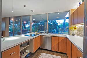 Kitchen with black electric cooktop, sink, dishwasher, light tile patterned floors, and a wall of windows