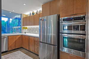 Kitchen with tile patterned floors, backsplash, sink, and appliances with stainless steel finishes