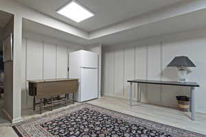 Basement with light wood-type flooring and white refrigerator