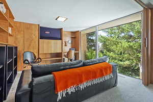 Carpeted living room featuring wood walls and floor to ceiling windows