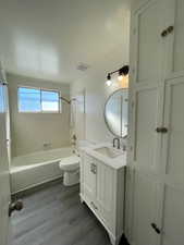 Full bathroom with vanity, tiled shower / bath combo, hardwood / wood-style floors, and toilet