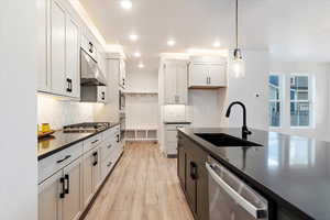 Kitchen with pendant lighting, sink, light hardwood / wood-style floors, white cabinetry, and stainless steel appliances