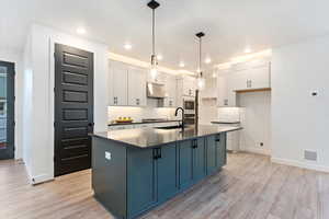 Kitchen with pendant lighting, light hardwood / wood-style flooring, white cabinetry, and a kitchen island with sink