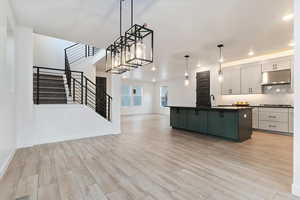 Kitchen with tasteful backsplash, a kitchen island with sink, hanging light fixtures, and light wood-type flooring