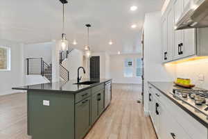 Kitchen featuring white cabinetry, wall chimney range hood, sink, and hanging light fixtures