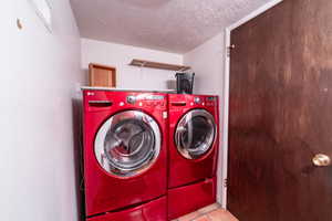 Washroom featuring washer and dryer, light tile patterned flooring, and a textured ceiling