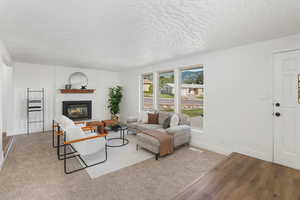 Living room with light wood-type flooring, a textured ceiling, a brick fireplace, and brick wall