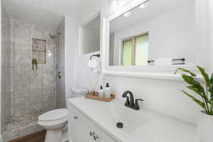 Bathroom with toilet, a tile shower, and vanity