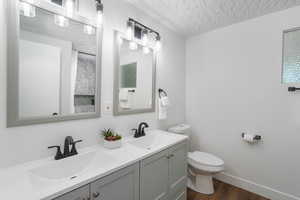 Bathroom with a textured ceiling, toilet, double vanity, and wood-type flooring