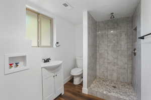 Bathroom with tiled shower, hardwood / wood-style flooring, toilet, and vanity