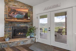 Doorway to outside with vaulted ceiling, hardwood / wood-style flooring, a stone fireplace, and french doors