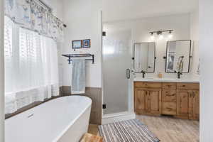 Primary Bathroom featuring tile walls, double vanity, independent shower and bath, and wood-type flooring