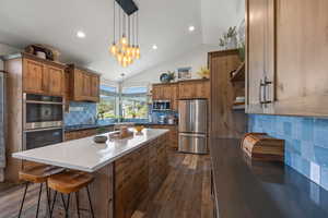 Kitchen featuring stainless steel appliances, dark hardwood / wood-style floors, tasteful backsplash, a kitchen island, and vaulted ceiling