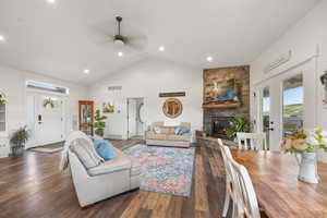 Living room with ceiling fan, dark hardwood / wood-style floors, high vaulted ceiling, and a stone fireplace